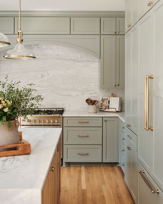 a sage green kitchen with shaker cabinets, a white quartz backsplash and countertops, pendant glass lamps