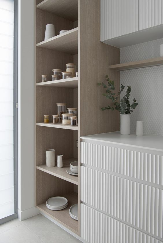 a serene kitchen with white ribbed drawers and cabinets, an open storage unit of light stained is an amazingly airy space