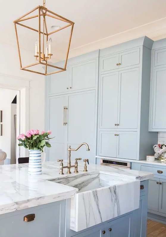 a serenity blue kitchen cabinets with white marble countertops and brass touches for a retro look