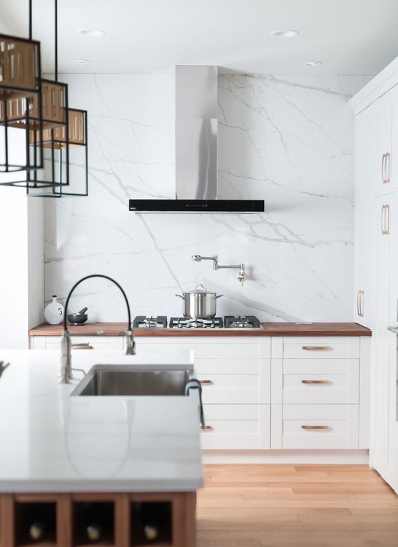 a small and cool white kitchen with shaker cabinets and a white quartz backsplash, butcherblock and quartz countertops