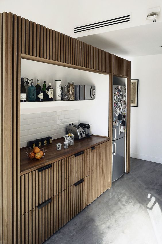 a small built in kitchen with ribbed built in cabinets, a white subway tile backsplash and an open shelf is cool