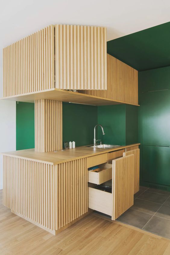 a small yet cool built-in kitchen with light-stained ribbed cabinets, a stained countertop that contrasts the emerald walls