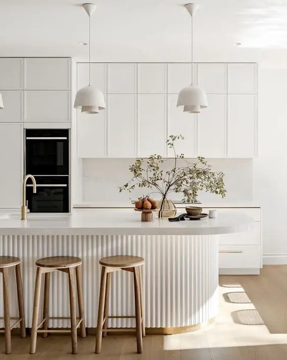 a sophisticated contemporary kitchen in white, with a white stone backsplash and countertops, a curved fluted kitchen island, pendant lamps