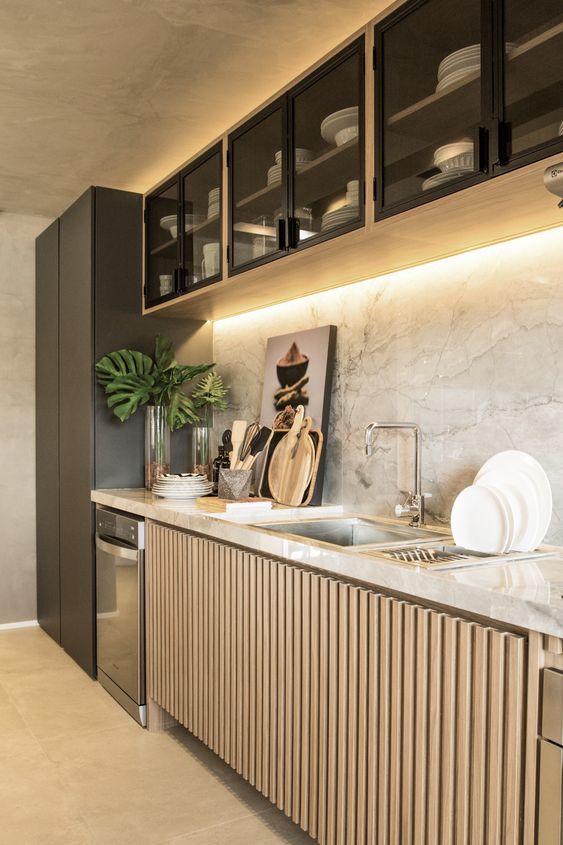a sophisticated contemporary kitchen with glass upper cabinets and fluted lower ones, a white stone backsplash and countertops