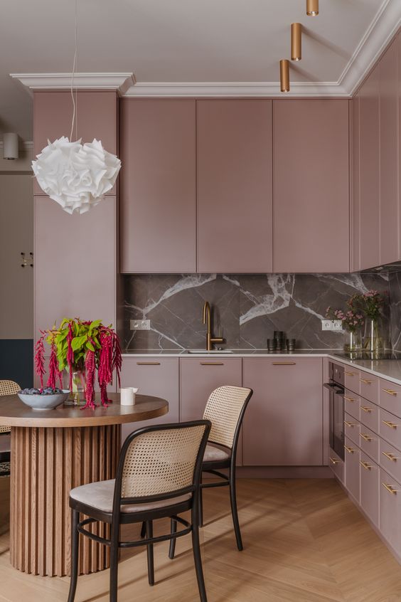 a sophisticated mauve kitchen with a grey marble backsplash and neutral countertops, copper lights and an eating zone