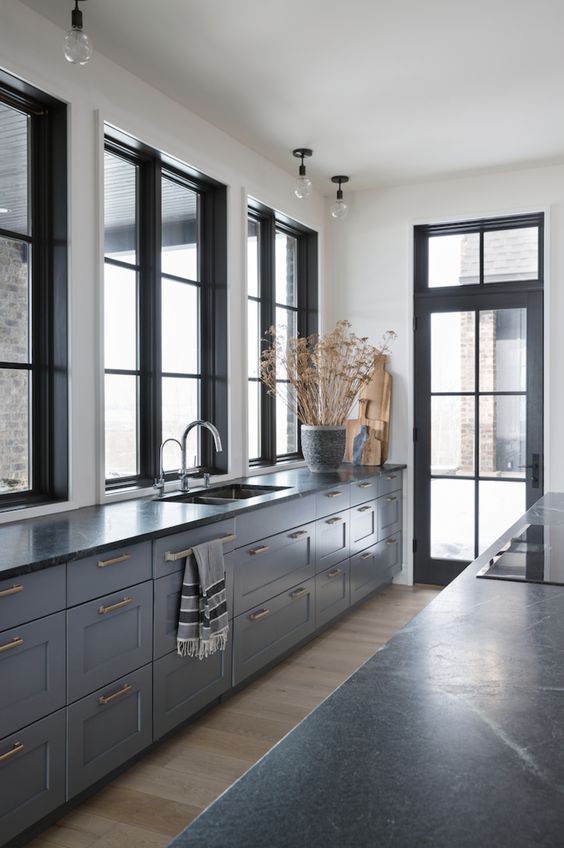 a stylish and elegant grey kitchen with shaker cbainets, black countertops, black framed windows and a door