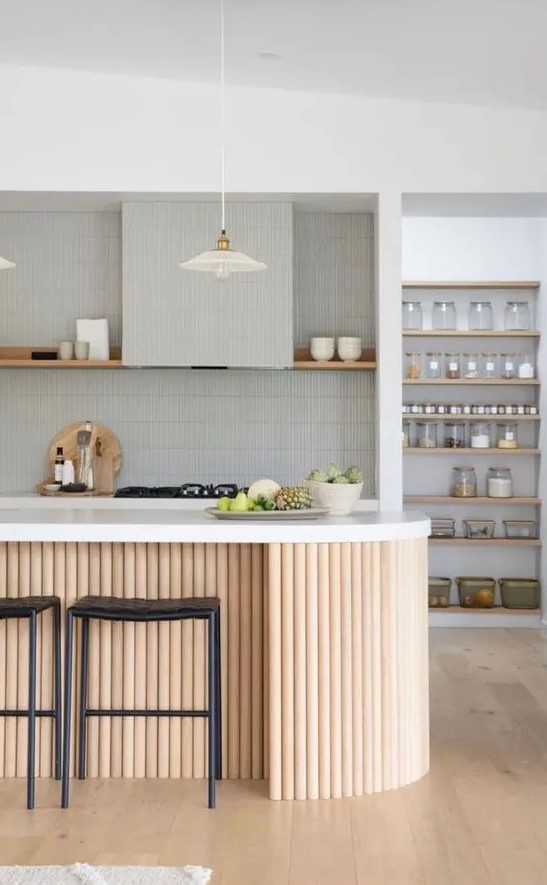 a stylish grey kitchen clad with skinny tile, with an open shelf instead of upper cabinets, an open pantry, a fluted curved kitchen island with a white stone countertop