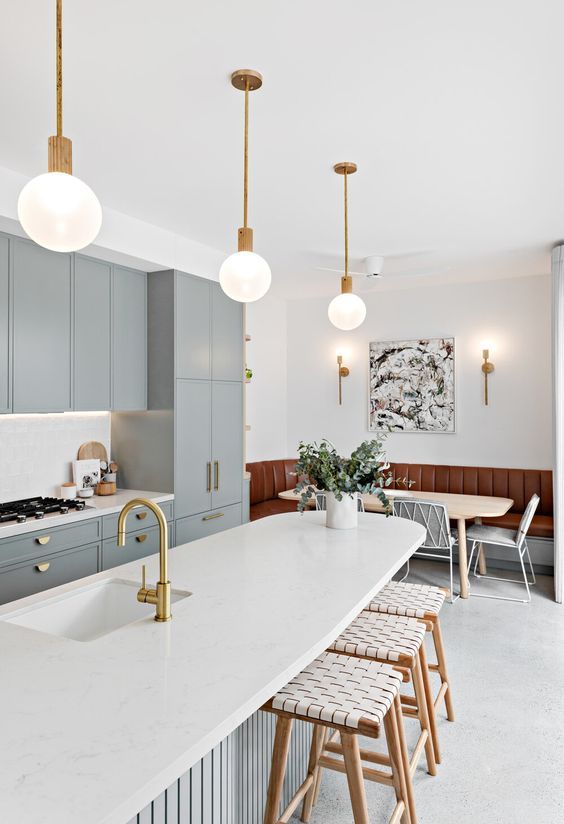 a stylish grey kitchen with gold handles, a curved kitchen island with a white countertop and cool pendant lamps