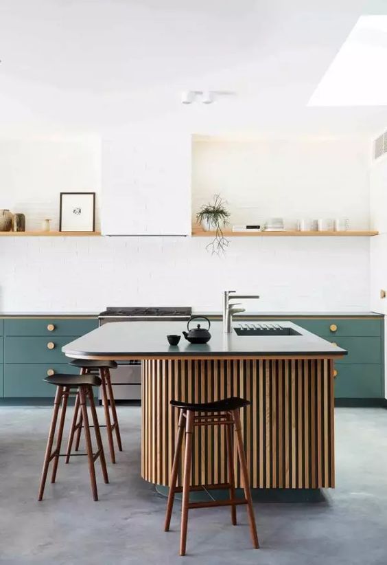 a stylish kitchen with green cabinetry, an open shelf instead of upper cabinets, a large fluted kitchen island with a black countertop and black stools