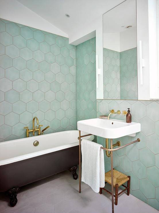 a stylish modern bathroom with green hexagon tiles, a black clawfoot tub, a white free-standing sink and a woven stool