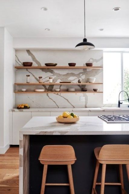 a stylish white kitchen with a navy kitchen island, a white quartz backsplash and countertops and open shelves