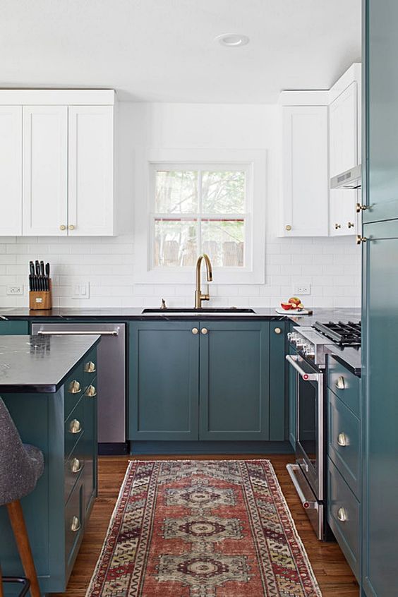 a two-tone hunter green and white kitchen with a white subway tile backsplash, black countertops and a bold printed rug