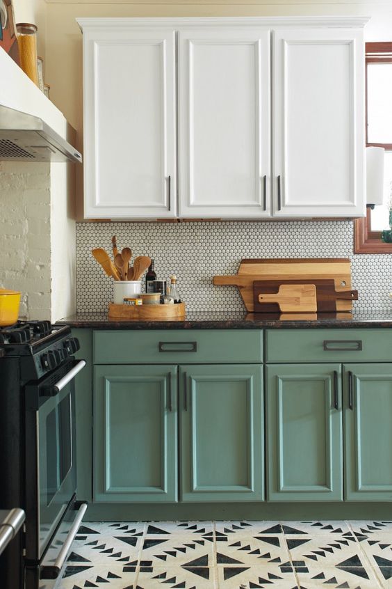 a two-tone kitchen with white and green shaker style cabinets, a pennyt tile backsplash and black countertops, a black and white tile floor