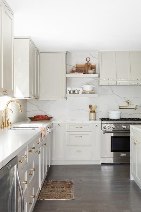 a very light grey kitchen with shaker cabinets, a white quartz backsplash and countertops and gold fixtures is pure elegance
