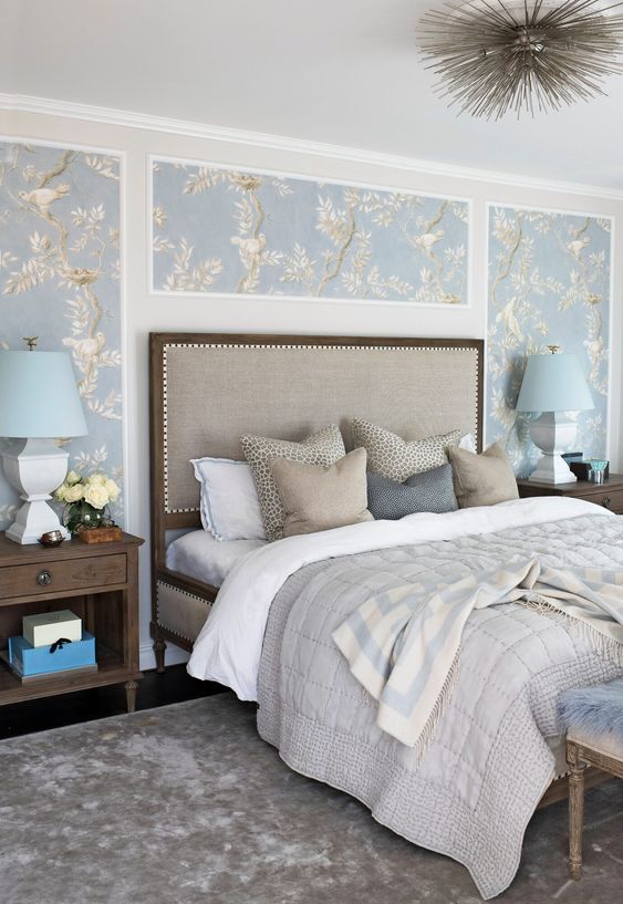 a vintage bedroom with blue printed wallpaper, an upholstered bed with neutral bedding, dark-stained nightstands