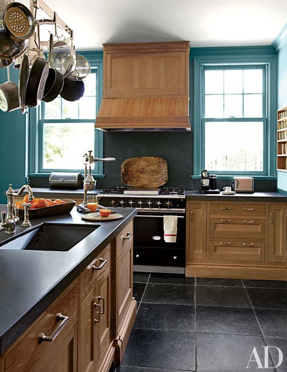 a vintage kitchen with stained cabinets, blue walls, a black backsplash and countertops plus a pan holder over the island