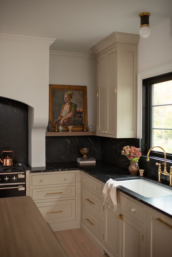 a vintage kitchen with tan shaker style cabinets, black marble countertops and a backsplash, some gold and brass touches