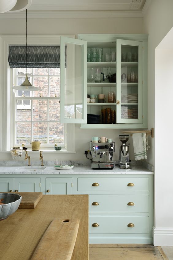 a vintage pastel green kitchen with a white stone countertops, glass door cabinets, vintage pendant lamps