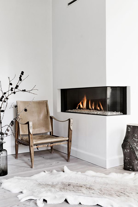 a welcoming Scandinavian space with a built-in corner fireplace, a leather and wood chair, a skin rug and some wild decor