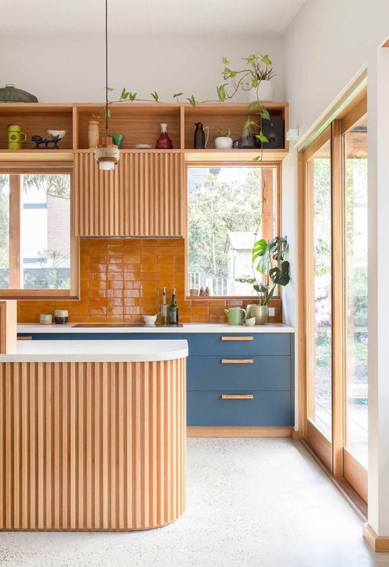 a welcoming warm-colored kitchen with blue cabinets, an orange backsplash and some light-stained cabinets, a curved kitchen island