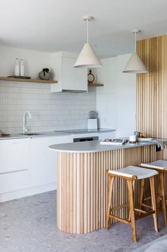 a white Scandinavian kitchen with grey stone countertops, open shelves, a fluted kitchen island and lamps over it