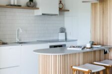 a white Scandinavian kitchen with grey stone countertops, open shelves, a fluted kitchen island and lamps over it