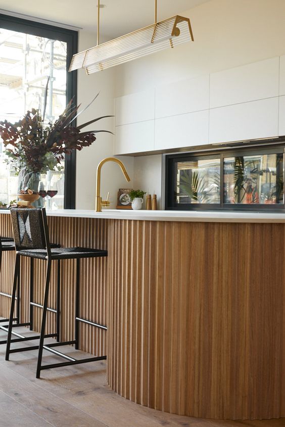 a white contemporary kitchen with sleek and plain cabinets, a window backsplash, a curved and fluted kitchen island as an accent here
