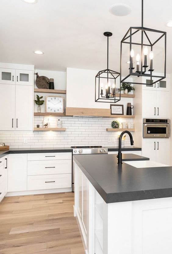 a white farmhouse kitchen with a white tile backsplash, open shelving, black countertops and fixtures for an accent
