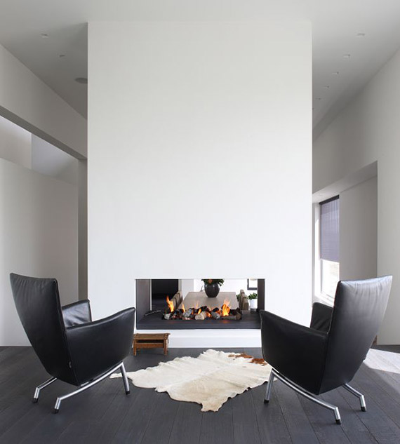 a white minimalist double sided fireplace, black leather chairs, a wooden stool and a skin rug are a perfect combo