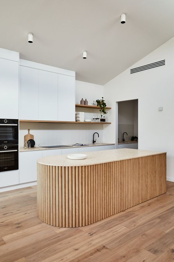 a white minimalist kitchen with a neutral stone countertop, a curved fluted kitchen island and open shelves