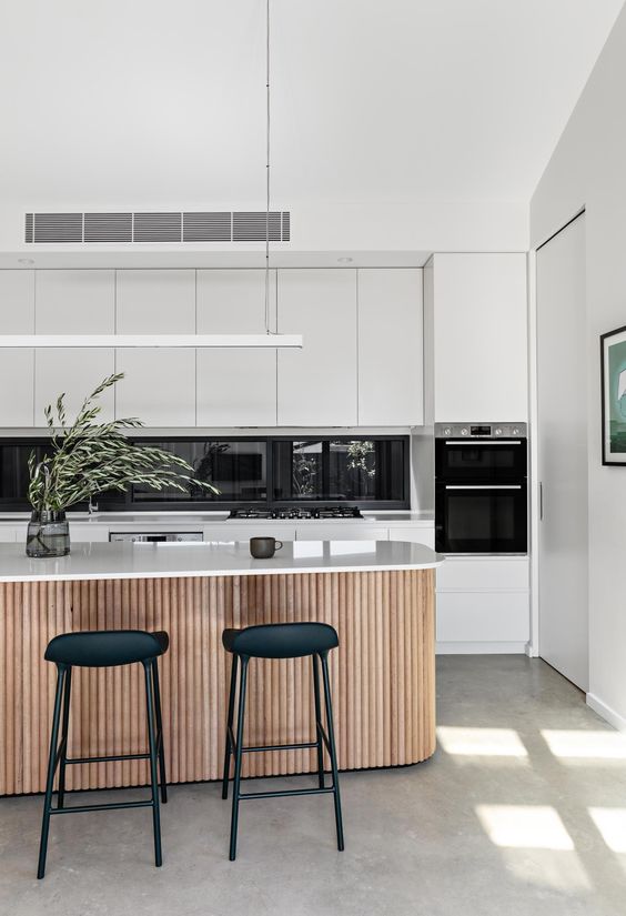 a white minimalist kitchen with a window backsplash, a large fluted kitchen island and sleek white countertops looks breezy