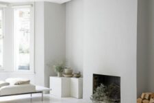 a white minimalist living room with a fireplace, cubes as side tables, a daybed, cushions and a firewood storage