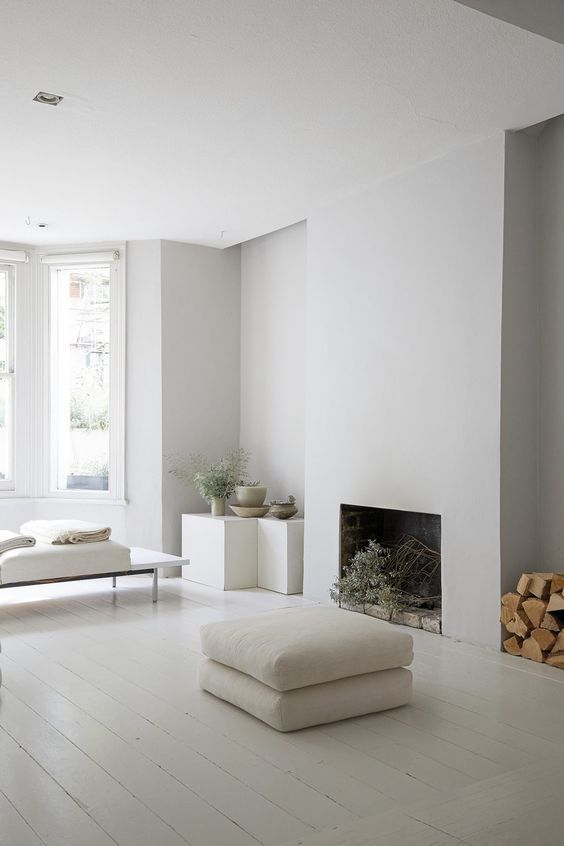a white minimalist living room with a fireplace, cubes as side tables, a daybed, cushions and a firewood storage