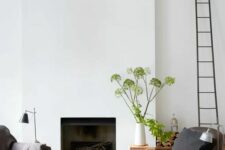 a wlecoming living room with a minimalist fireplace, a couple of chairs, greenery, a ladder and a black lamp
