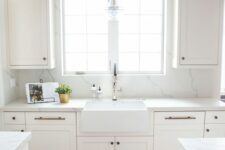 an airy white kitchen with shaker cabinets, a white quartz backsplash and countertops plus brass fixtures is wow