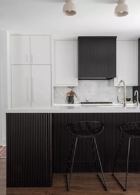 an elegant and laconic black and white kitchen with white and black reeded cabinets and a matching kitchen island plus black stools