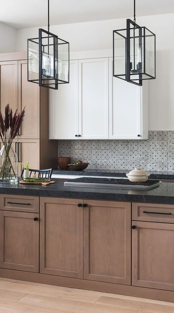 an elegant farmhouse kitchen with stained and white cabinets, a black and white tile backsplash and black countertops plus black framed lamps