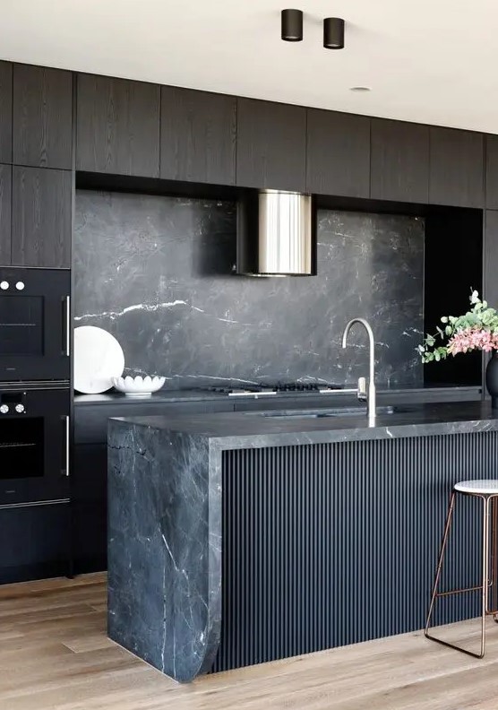 an exquisite kitchen with dark-stained cabinets, a black fluted kitchen island, a black marble backsplash and countertops