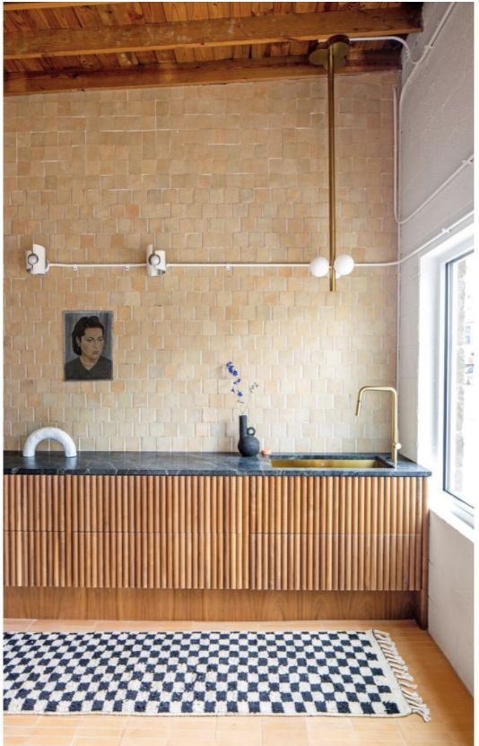 an eye-catchy kitchen with flated lower cabients and a black marble countertop, a tan and beige Zellige tile wall and some art
