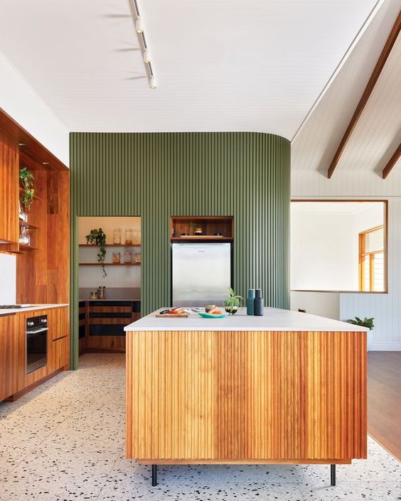 an eye catchy mid century modern kitchen with stained cabinets, a robust fluted kitchen island and a matching fluted curved green wall