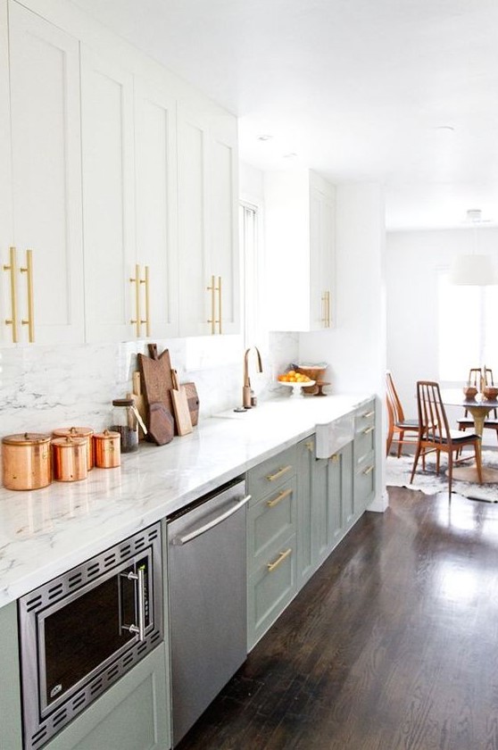 an inviting mid-century modern kitchen with light green and white cabinets, a white stone backsplash and countertops, gold touches