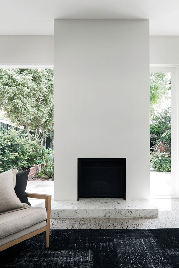 an ultra-minimalist space with a white fireplace with a marble detail, a black rug and a neutral chair plus a garden view