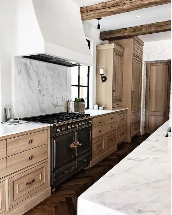 a beautiful and refined kitchen with light-stained cabinetry, a white hood and a white marble backsplash plus countertops