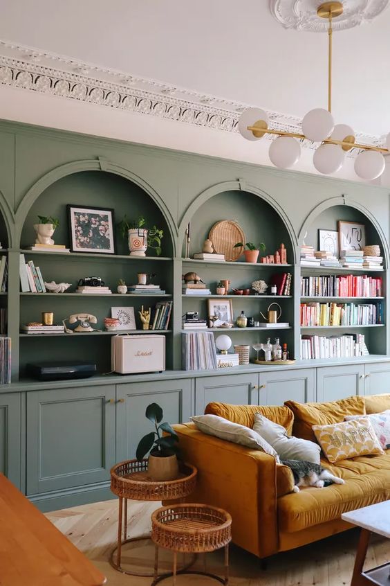 https://www.digsdigs.com/photos/2023/02/02-a-chic-living-room-with-a-sage-green-accent-wall-with-built-in-niches-and-storage-units-a-mustard-sofa-rattan-side-tables-and-lovely-colorful-niche-decor.jpg