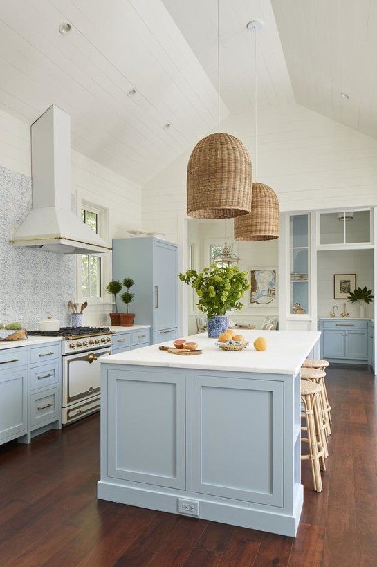 a beautiful coastal kitchen in light blue and white, with a mosaic tile backsplash, wicker lampshades and rattan stools plus greenery