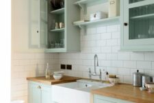 03 a chic mint green farmhouse kitchen with shaker style cabinets, butcherblock countertops, a white subway tile backsplash and a vintage faucet