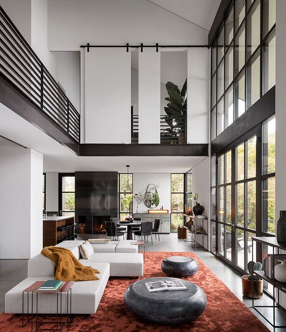 a contemporary living room with a glazed framed wall, a white sofa, black coffee tables, some side tables and a coral rug