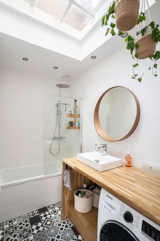 a modern black and white bathroom with a skylight, a bathtub, a timber vanity with a built-in washing machine and a round mirror