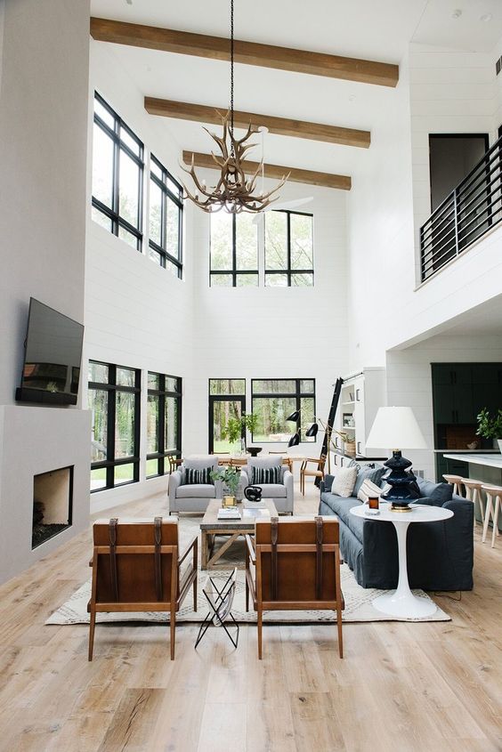 a contemporary living room with two rows of windows, a grey and a navy sofa, neutral chairs, a coffee table and an anterl chandelier