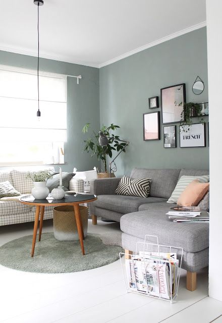 a Scandinavian living room with sage gree walls, a windowpane print and grey sofa, printed pillows, a gallery wall and a coffee table